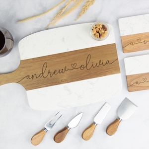 May include: A white and wood serving board with the names "andrew & olivia" engraved. Includes matching coasters and cheese knives. The board is 16 inches long.