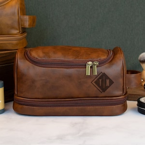 May include: Brown leather travel toiletry bag with a zipper closure and a monogrammed leather patch that says "T|N".