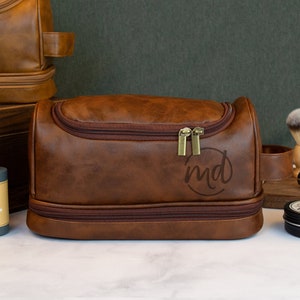 May include: Brown leather travel toiletry bag with a zipper closure and a monogrammed "md" on the front. The bag has a brown leather handle and a second zippered compartment.