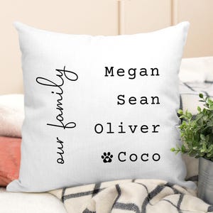 May include: White throw pillow with black text that reads "our family" and the names Megan, Sean, Oliver, and Coco with a paw print symbol.