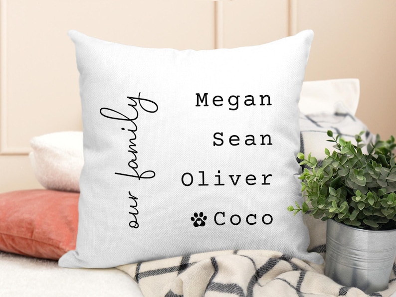 May include: White throw pillow with black text that reads "our family" and the names Megan, Sean, Oliver, and Coco with a paw print symbol.