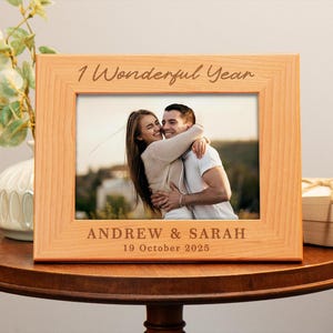 May include: A wooden photo frame with a couple in a photo. The frame has the text "1 Wonderful Year" and "Andrew & Sarah 19 October 2025" engraved on it.