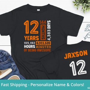 May include: Black t-shirt with orange text that reads "12 Years 105,192 Hours 6,311,520 Minutes of Being Awesome" and "144 Months 4,383 Days". The back of the shirt has the name "Jaxson" and the number "12" in white.