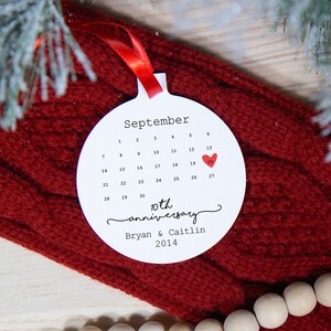 May include: White round ornament with a calendar for September with a red heart on the 20th. The text reads "10th anniversary Bryan & Caitlin 2014".