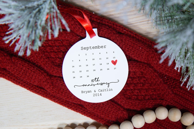 May include: White round ornament with a calendar for September with a red heart on the 20th. The text reads "10th anniversary Bryan & Caitlin 2014".