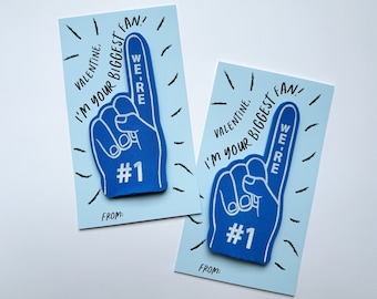 May include: Two blue foam finger cards with the text "I'm your biggest fan!" and "We're #1" on them. The cards are on a light blue background.