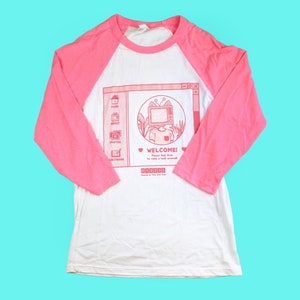 May include: White and pink raglan baseball tee with a graphic on the front. The graphic features a retro computer window design with a cat wearing a TV head. Text on the graphic reads "WELCOME!" and "Please feel free to make a little around!"