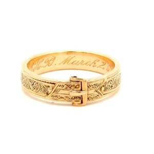 Könnte beinhalten: Ein goldfarbenes, graviertes, Scharnier-Armband mit einer Schließe. Die Inschrift "18. March 2." ist auf der Innenseite des Armbands eingraviert.