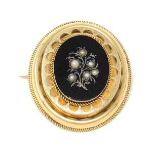 May include: A gold oval brooch with a black enamel center featuring a floral design with pearl accents.