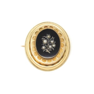 May include: A gold oval brooch with a black enamel center featuring a floral design with pearl accents.