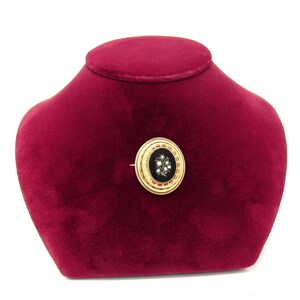 May include: A gold brooch with a black enamel center and a cluster of white pearls in the shape of a flower.