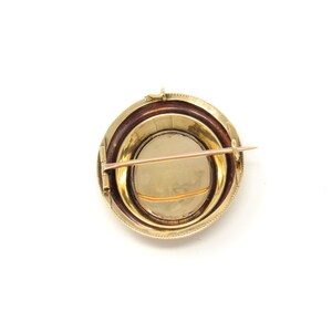 May include: A gold oval-shaped brooch with a decorative border and a pin on the back.