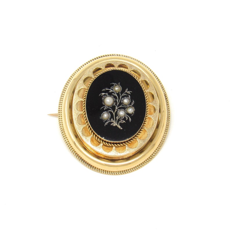 May include: A gold oval brooch with a black enamel center featuring a floral design with pearl accents.