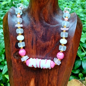 Op de afbeelding: Een roze en witte glazen kralenketting met een dikke witte en roze swirl kraal in het midden.