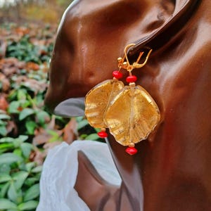 May include: Gold leaf earrings with red glass beads. The earrings are shaped like leaves and have a textured surface.