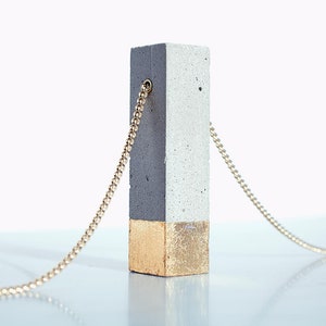 May include: A gray concrete pendant with a gold bottom half, hanging from a gold chain.