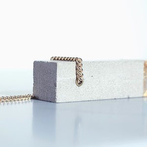 May include: A concrete pendant necklace with a gold accent and a gold chain. The pendant is rectangular and has a rough texture.