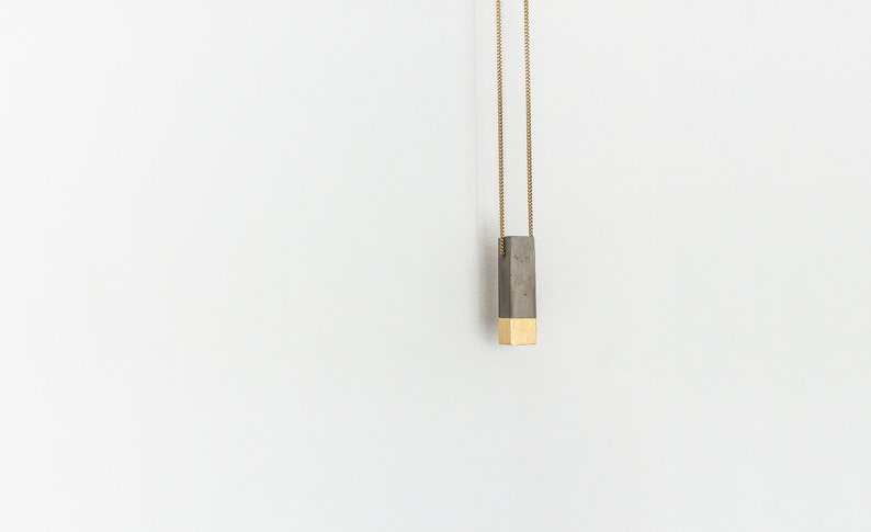 May include: A gold chain necklace with a rectangular pendant made of gray concrete and gold metal.