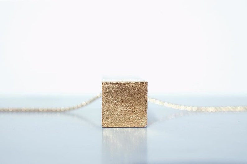 May include: A gold necklace with a square pendant. The pendant is made of a textured material that looks like gold leaf.