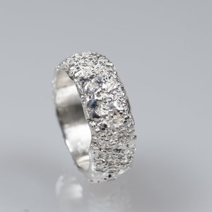 Op de afbeelding: Een zilveren ring met een getextureerd oppervlak. De ring is breed en heeft een afgeronde vorm.