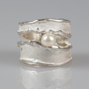 May include: A silver ring with a textured, organic design. A single white pearl is set in the center of the ring.