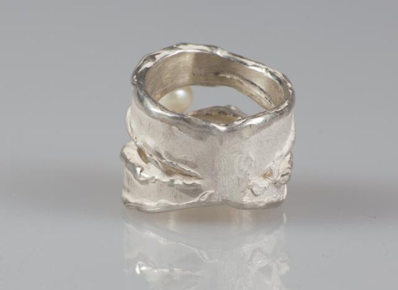 May include: A silver ring with a textured, organic design. The ring has a pearl set into the band.