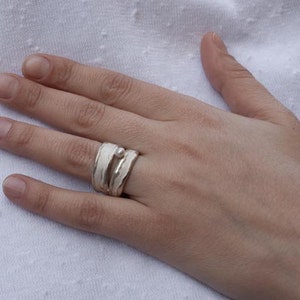 May include: A silver ring with a white enamel design. The ring is worn on the middle finger of a hand.