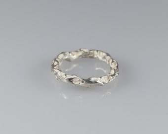 May include: A silver ring with a textured, organic design. The ring is made of a single piece of metal and has a rough, uneven surface.