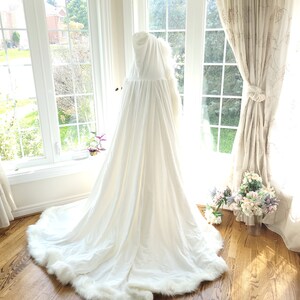 May include: A white hooded cape with a faux fur trim. The cape is made of a soft, flowing fabric and has a long, elegant train.