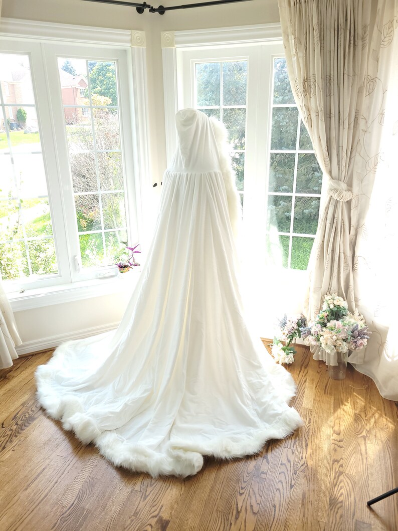 May include: A white hooded cape with a faux fur trim. The cape is made of a soft, flowing fabric and has a long, elegant train.