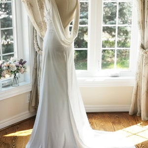 May include: A white wedding dress with a low back and a flowing train. The dress is made of a smooth, silky fabric and has a simple, elegant design.