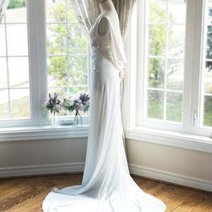May include: A white wedding dress with a fitted bodice and a flowing skirt. The dress has a lace overlay on the bodice and a small train. The dress is displayed on a mannequin against a white background.