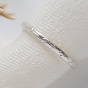 May include: A silver ring with a textured design. The ring is on a white fabric background.