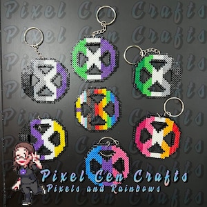 Puede incluir: Siete llaveros diferentes con el signo de la paz hechos con cuentas perler de colores. Cada llavero presenta un esquema de colores diferente, incluyendo negro, blanco, verde, morado, amarillo, rosa, azul y colores del arcoíris. Los llaveros se muestran sobre una superficie negra con el texto "Pixel Cen Crafts" y "Pixels and Rainbows" visible debajo.