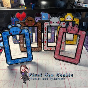 Puede incluir: Una colección de marcos de fotos de cuentas coloridas en varios diseños. Los marcos presentan adornos de personajes de dibujos animados y patrones florales. Los marcos son en tonos de azul, marrón, rosa, blanco y amarillo. El texto "Pixel Con Crafts" es visible.