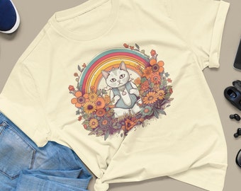 Puede incluir: Un gato blanco con un arcoíris detrás, sentado en un campo de flores. El gato lleva una camisa azul y blanca con un corazón. Las flores son de color amarillo, naranja y rosa.