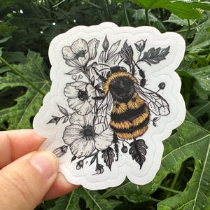 May include: A black and white illustration of a bumblebee surrounded by flowers. The bumblebee is yellow and black with fuzzy hairs. The flowers are white with black centers.