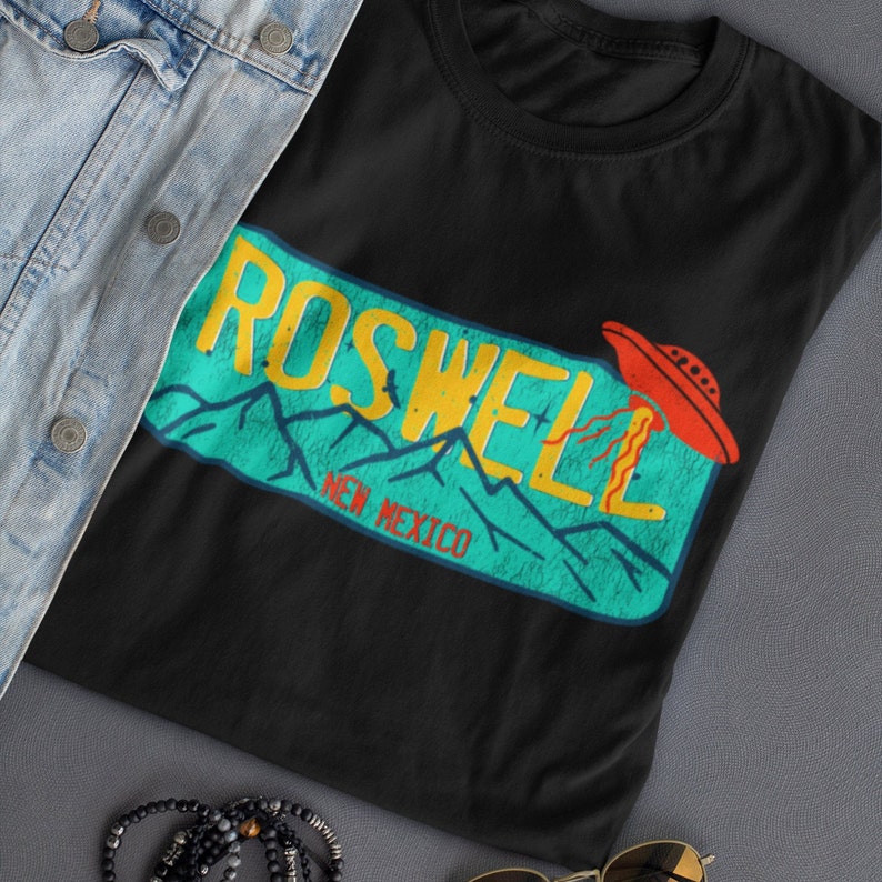 May include: Black t-shirt with a retro-style graphic of a UFO over a mountain range with the text "Roswell, New Mexico".