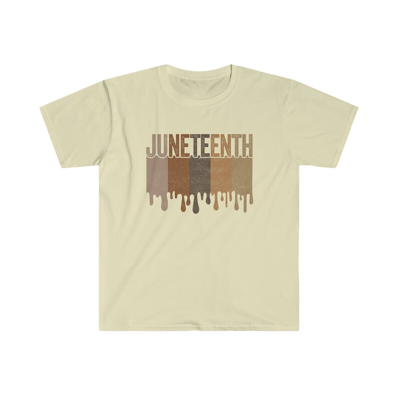 May include: A beige t-shirt with a graphic print of the word "JUNETEENTH" in brown, tan, and dark brown letters. The letters are dripping with paint, creating a dripping effect.