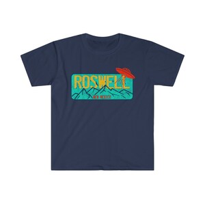 May include: A navy blue t-shirt with a graphic of a vintage license plate that says "Roswell, New Mexico" with a red UFO flying over the mountains.