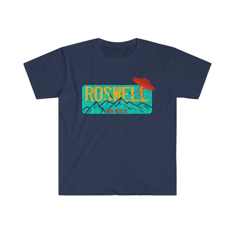 May include: A navy blue t-shirt with a graphic of a vintage license plate that says "Roswell, New Mexico" with a red UFO flying over the mountains.