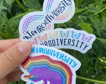 Könnte beinhalten: Drei Aufkleber mit den Worten "Neurodiversität" und "Neurodiversitätsbewusstsein" in einem Regenbogen-Farbschema. Der erste Aufkleber zeigt ein Unendlichkeitszeichen mit Herzen. Der zweite Aufkleber zeigt einen Regenbogen mit Schmetterlingen. Der dritte Aufkleber zeigt eine Bärensilhouette mit einem Regenbogen.