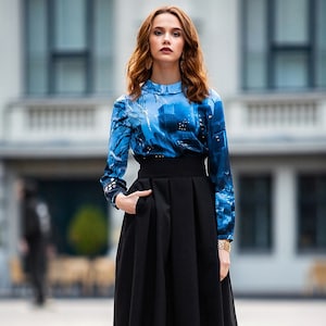 Pu&ograve; includere: Una donna indossa una blusa a maniche lunghe con motivo blu e bianco, una gonna nera a vita alta e stivaletti grigi.