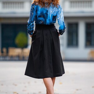 Pu&ograve; includere: Una donna indossa una blusa con motivo blu e bianco, una gonna nera e stivaletti grigi.