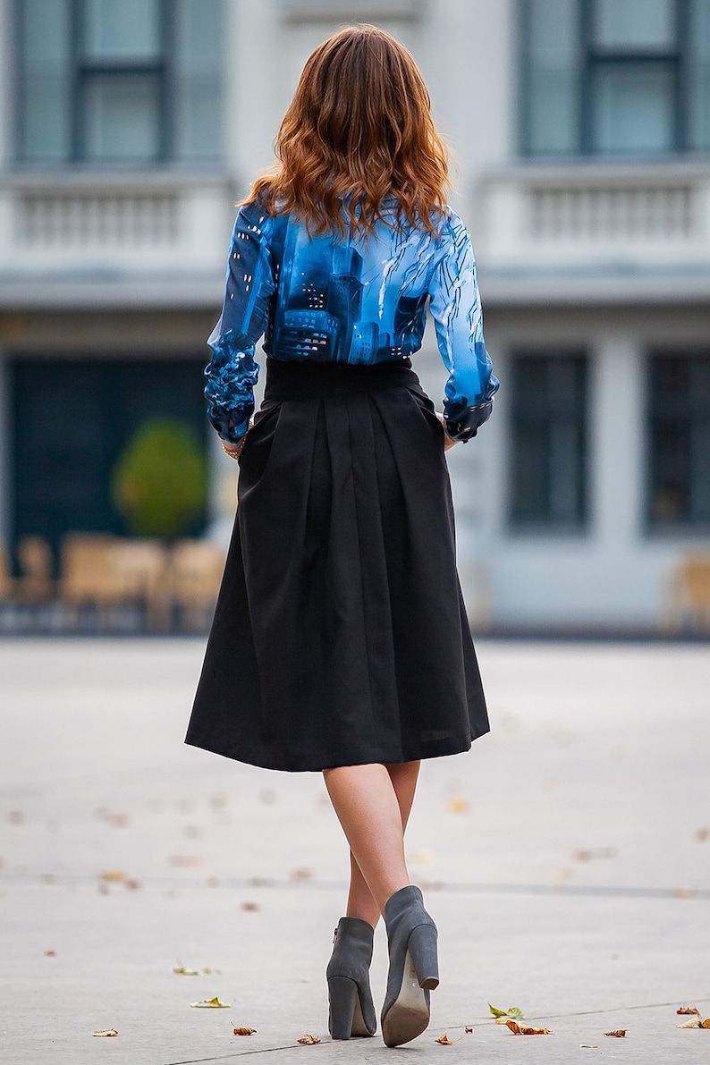 Pu&ograve; includere: Una donna indossa una blusa con motivo blu e bianco, una gonna nera e stivaletti grigi.
