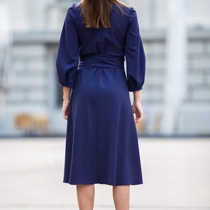 May include A navy blue midi dress with a wrap-style waist and long sleeves. The dress has a slightly flared skirt and is worn with burgundy ankle boots.