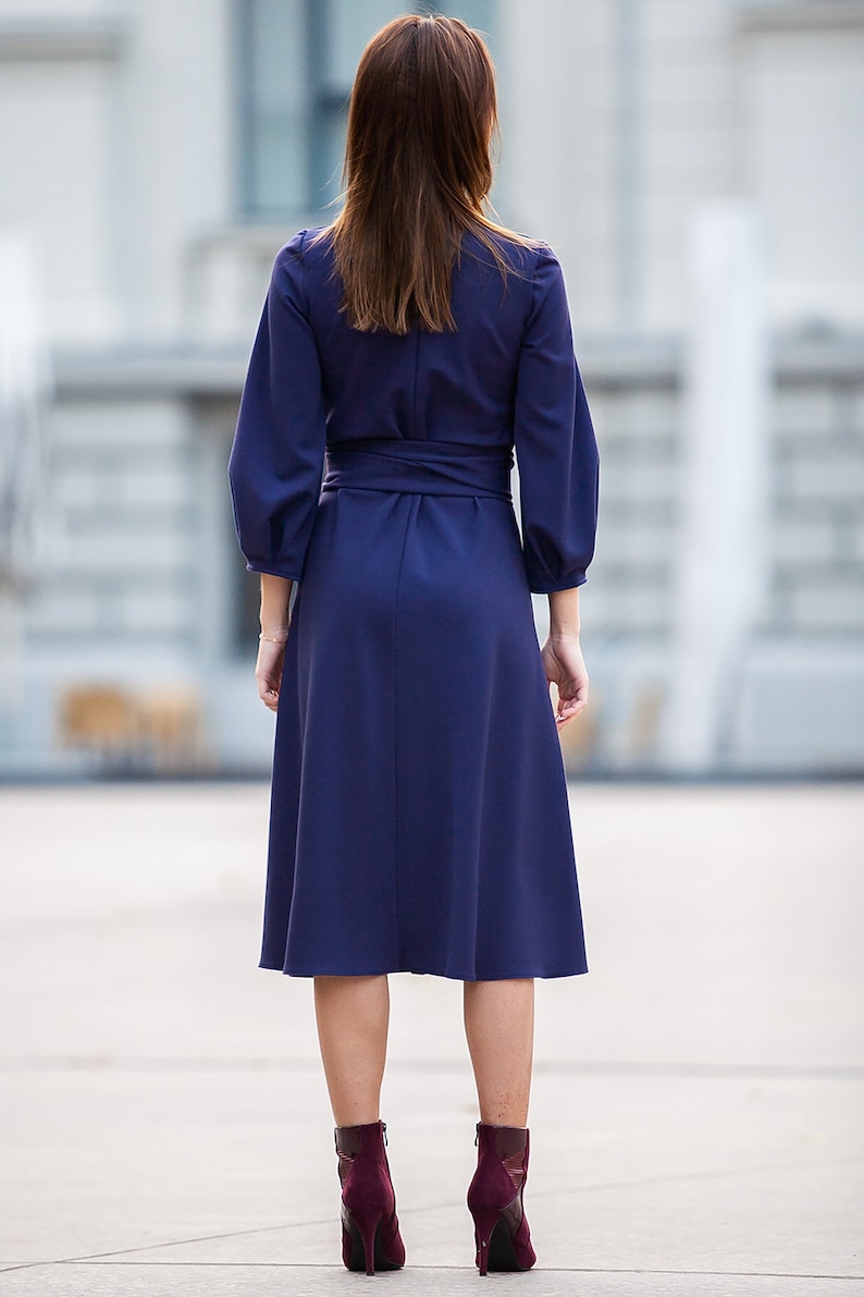 May include A navy blue midi dress with a wrap-style waist and long sleeves. The dress has a slightly flared skirt and is worn with burgundy ankle boots.