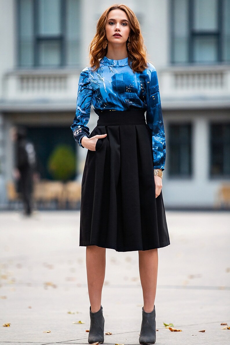 Pu&ograve; includere: Una donna indossa una blusa a maniche lunghe con motivo blu e bianco, una gonna nera a vita alta e stivaletti grigi.