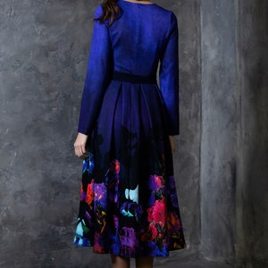 K&ouml;nnte beinhalten: Ein lang&auml;rmeliges Kleid mit einem blauen Oberteil und einem schwarzen und violetten Rock mit Blumenmuster. Das Kleid hat ein figurbetontes Oberteil und einen vollen Rock.