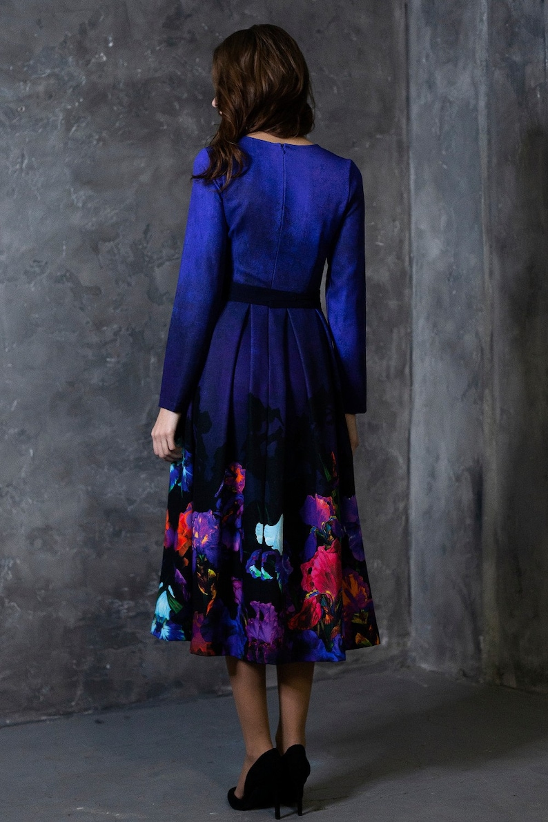 K&ouml;nnte beinhalten: Ein lang&auml;rmeliges Kleid mit einem blauen Oberteil und einem schwarzen und violetten Rock mit Blumenmuster. Das Kleid hat ein figurbetontes Oberteil und einen vollen Rock.